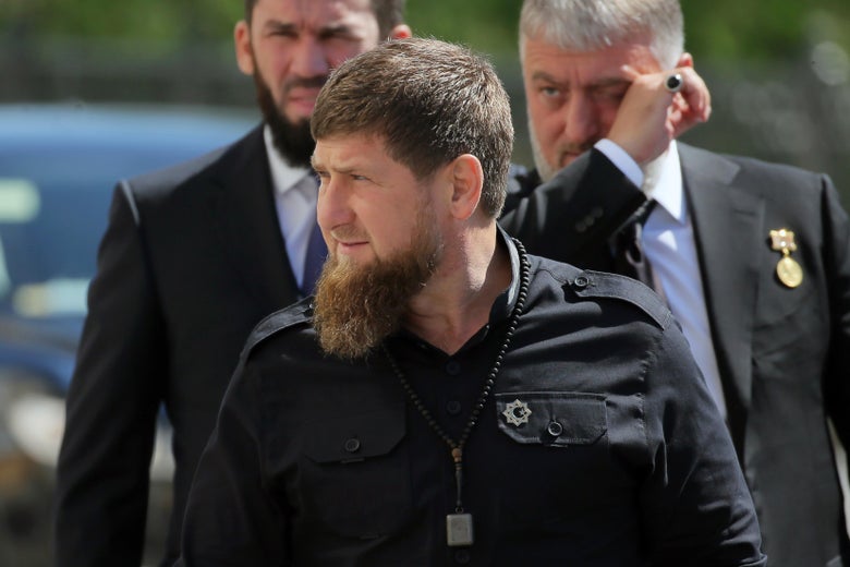 Ramzan Kadyrov, wearing a black shirt and a bushy beard, stands in front of two other men.